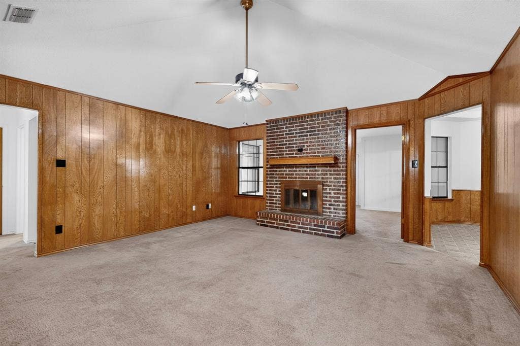 303 Stoneybrook Drive, Wylie, TX 75098 Vaulted ceiling with a ceiling fan, brick fireplace with a wood mantle, wood paneling, and carpet flooring