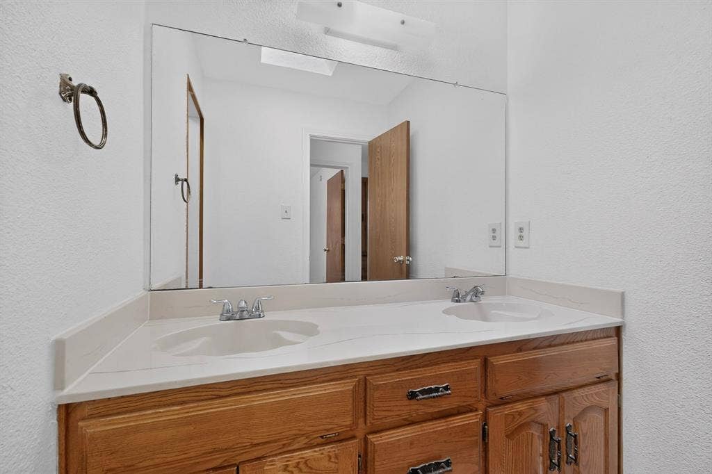 303 Stoneybrook Drive, Wylie, TX 75098 Dual vanity with integrated sinks, wood-finish cabinetry, and a full-width mirror