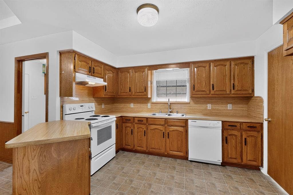 303 Stoneybrook Drive, Wylie, TX 75098 Kitchen featuring wood-finish cabinetry, a double basin sink, a built-in dishwasher, and a white electric range with an overhead exhaust hood