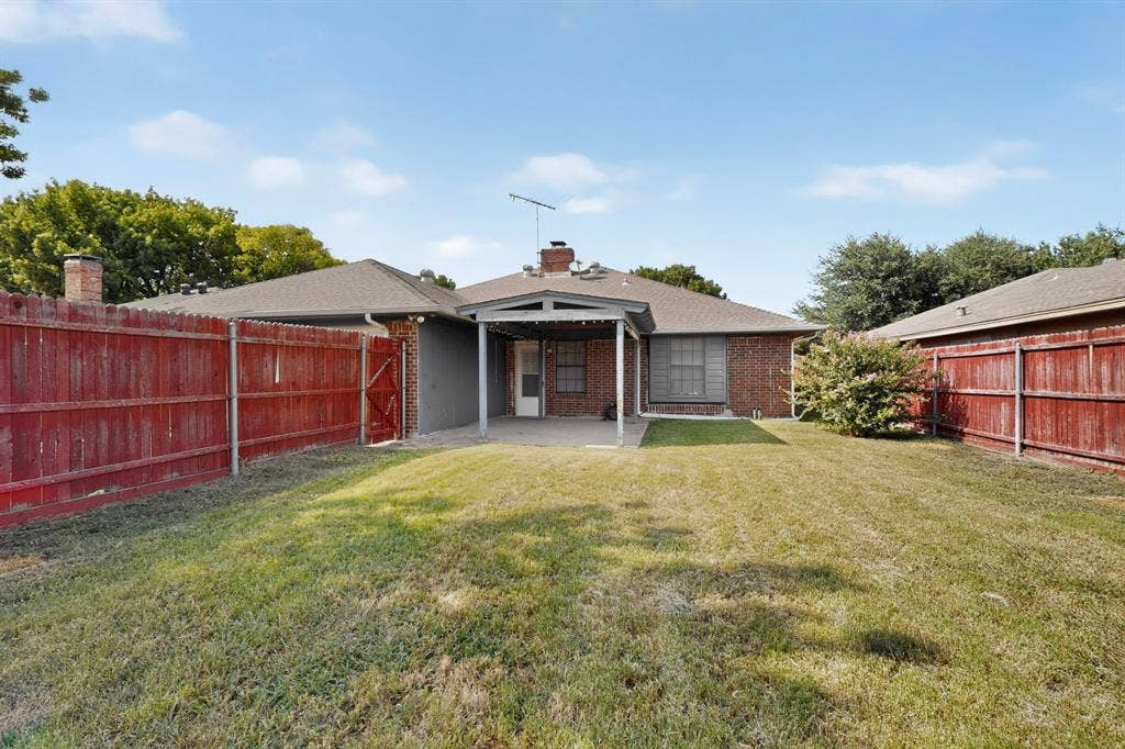 303 Stoneybrook Drive, Wylie, TX 75098 Expansive backyard with a covered patio, red-stained wood privacy fence, and brick exterior