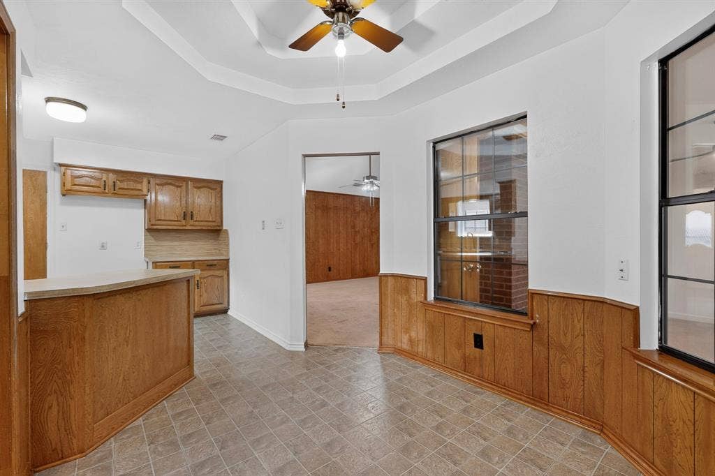 303 Stoneybrook Drive, Wylie, TX 75098 Tray ceiling with a ceiling fan, wood-finish kitchen cabinetry, breakfast bar, and wood paneling
