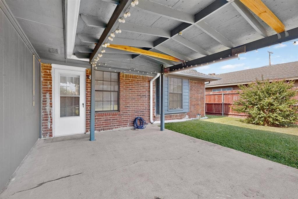 303 Stoneybrook Drive, Wylie, TX 75098 Covered patio with a concrete surface, supported by exposed wood beams, brick exterior, and a manicured lawn