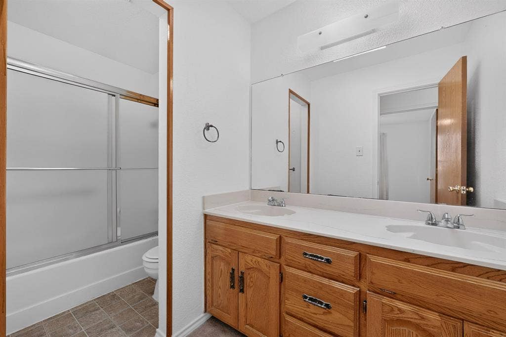 303 Stoneybrook Drive, Wylie, TX 75098 Double vanity with dual sinks, warm wood-finish cabinetry, and a large wall-mounted mirror