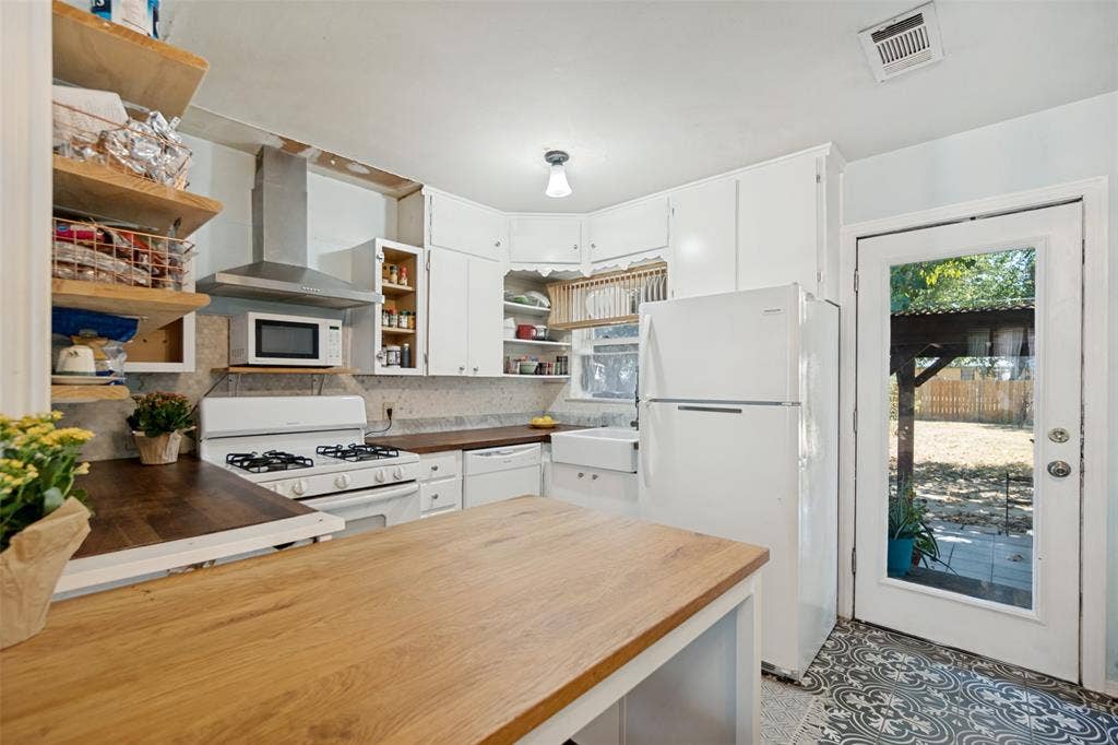 2312 Brooks Street, Garland, TX 75041 Kitchen with white cabinetry, wood-finish countertops, stainless steel range hood, and patterned floor tiling