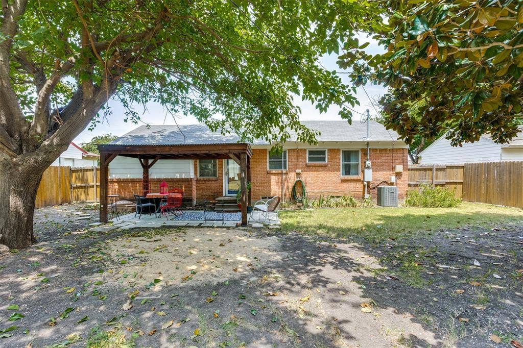 2312 Brooks Street, Garland, TX 75041 Expansive backyard featuring a wood pergola over a paved patio, mature trees, and a privacy fence