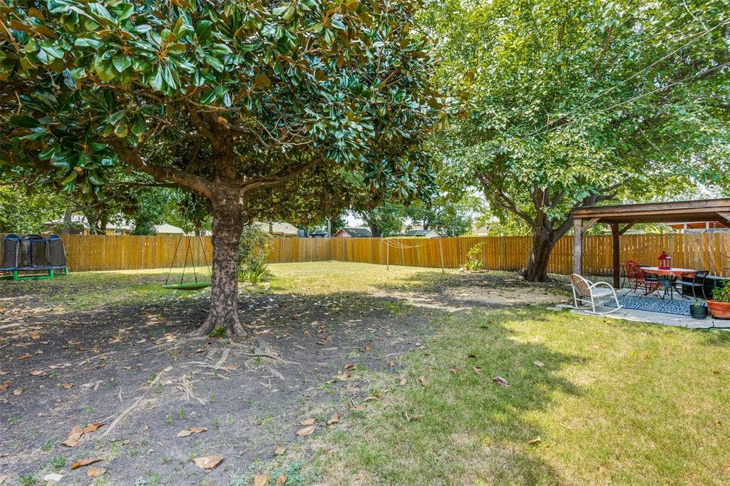 2312 Brooks Street, Garland, TX 75041 Expansive backyard featuring a wood privacy fence, mature trees, and a covered patio with a wooden pergola