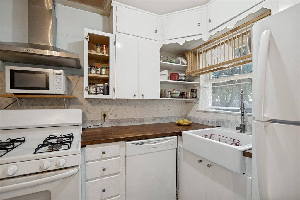 2312 Brooks Street, Garland, TX 75041 White cabinetry, wood-finish countertops, stainless steel range hood, built-in dishwasher, and a farmhouse-style sink