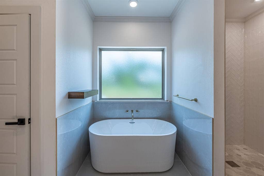 17049 Island Lake Drive, Tyler, TX 75708 Freestanding soaking tub with a wall-mounted faucet, complemented by a wood-finish floating shelf