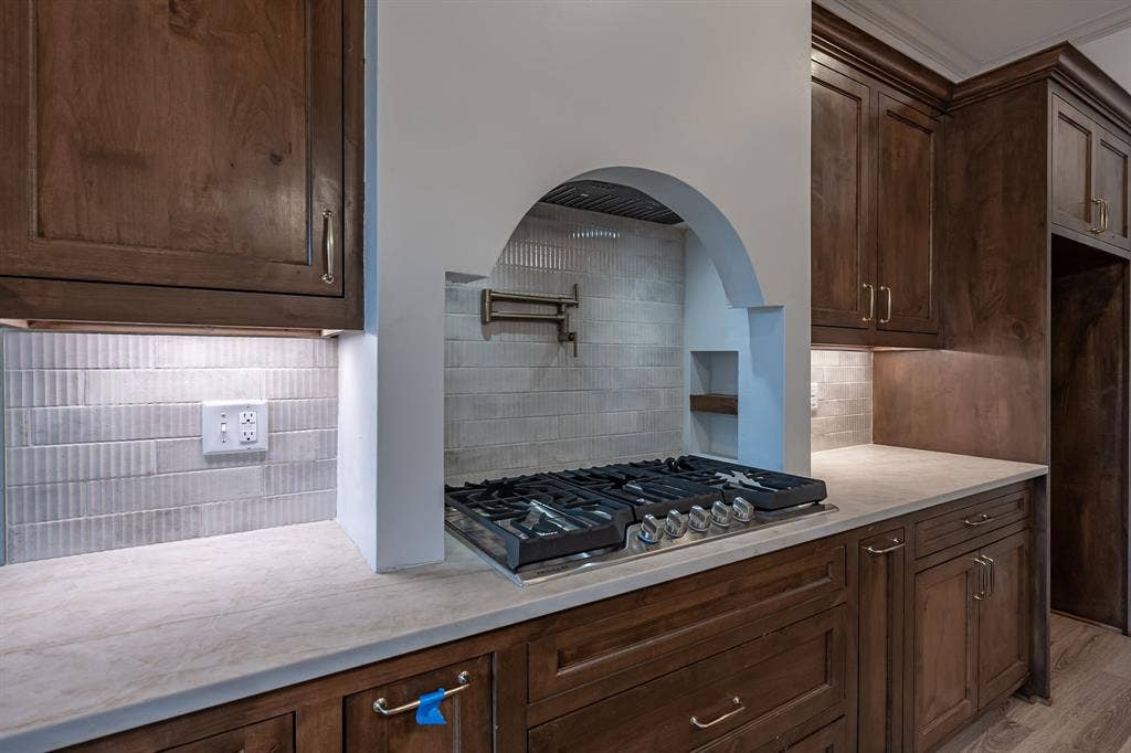 17049 Island Lake Drive, Tyler, TX 75708 Built-in gas range, arched range hood, wood cabinetry, light-toned countertops, and mosaic tile backsplash