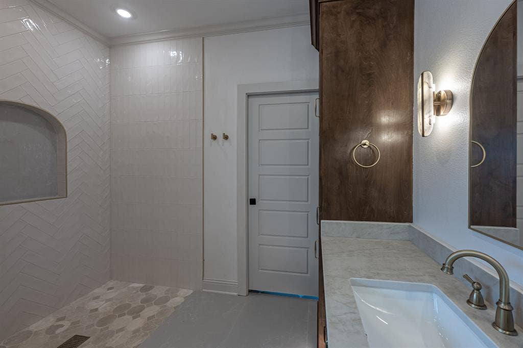 17049 Island Lake Drive, Tyler, TX 75708 Herringbone-patterned shower wall tile with integrated niche, hexagonal shower floor tile, vanity with integrated sink, brushed metal faucet, and dark wood-finish cabinetry