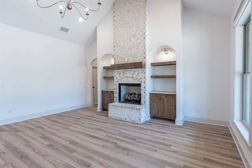 17049 Island Lake Drive, Tyler, TX 75708 Vaulted ceiling with an ornate chandelier, fireplace with brick surround, built-in shelving and cabinetry, and wood-finish flooring