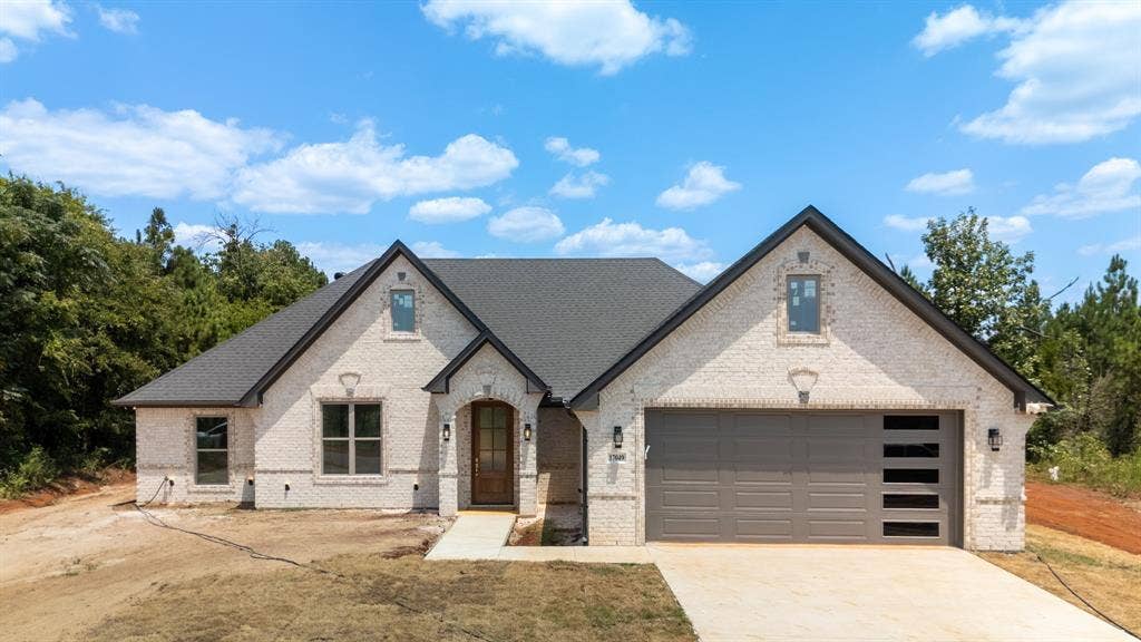 17049 Island Lake Drive, Tyler, TX 75708 White brick exterior with dark shingle roofing, prominent gables, an arched wood entry door, and a two-car garage with frosted glass inserts