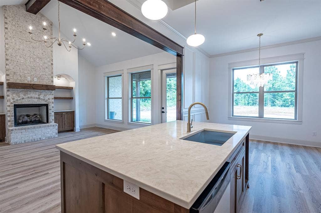 17049 Island Lake Drive, Tyler, TX 75708 Vaulted ceiling with exposed wood beams, stone fireplace, built-in shelving, wood-finish flooring, and a kitchen island with integrated sink