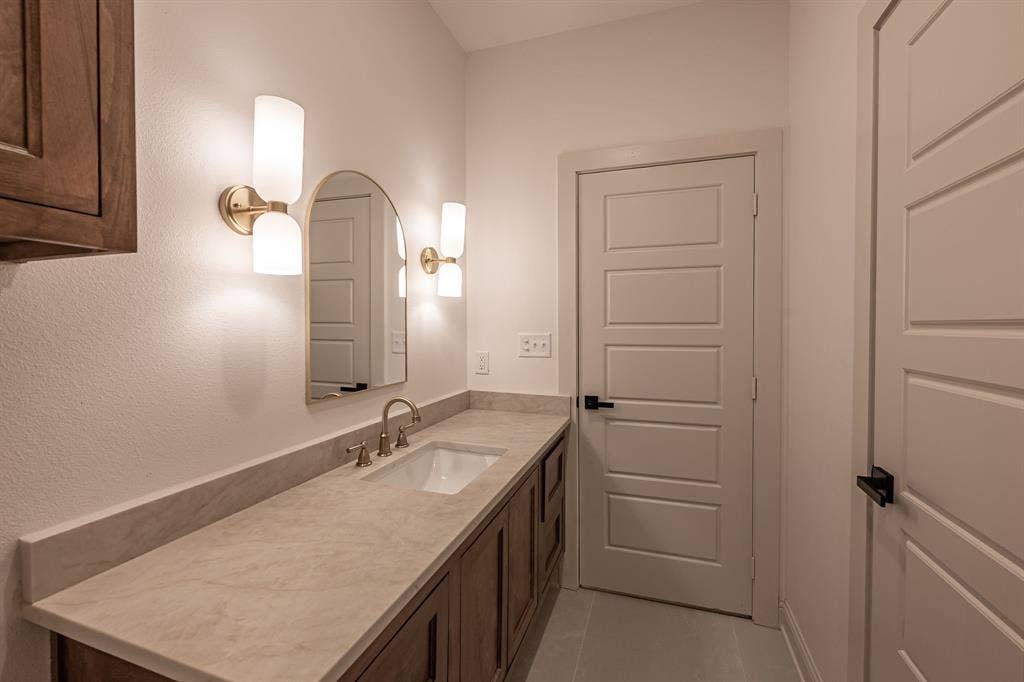 17049 Island Lake Drive, Tyler, TX 75708 Long single vanity with an integrated sink, brushed gold faucet, and a large arched mirror