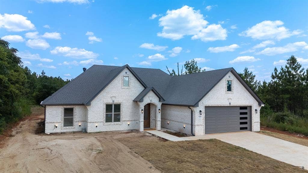 17049 Island Lake Drive, Tyler, TX 75708 White brick exterior with dark shingle roof, arched entry, concrete driveway, and a modern garage door with frosted panels