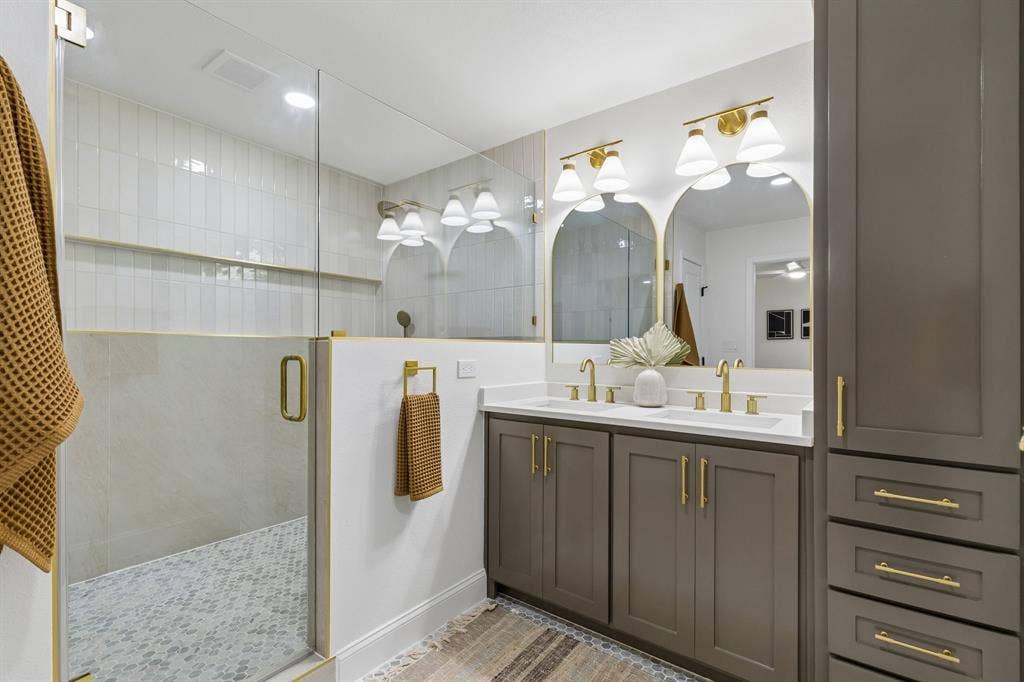 12124 Dixfield Drive, Dallas, TX 75218 Glass-enclosed shower with gold-tone hardware, dual vanity with undermount sinks, and integrated storage cabinetry