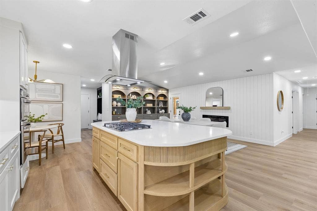 12124 Dixfield Drive, Dallas, TX 75218 Gourmet kitchen featuring a curved wood-finish island with open shelving, white quartz countertops, stainless steel range hood, gas cooktop, and recessed lighting throughout