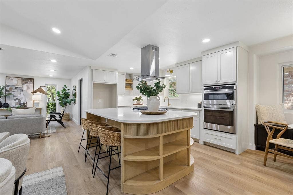 12124 Dixfield Drive, Dallas, TX 75218 Central kitchen island with wood-finish shelving, stainless steel appliances, white cabinetry, and wood-finish flooring