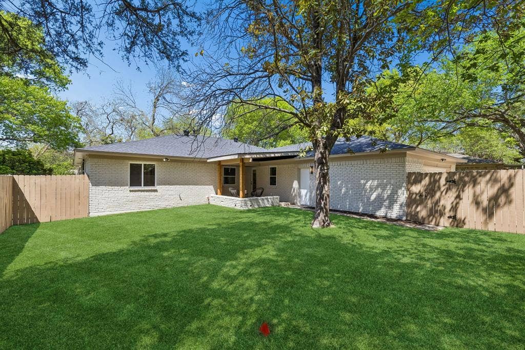 12124 Dixfield Drive, Dallas, TX 75218 Expansive fenced backyard featuring a manicured lawn, mature trees, and a covered patio with wood columns