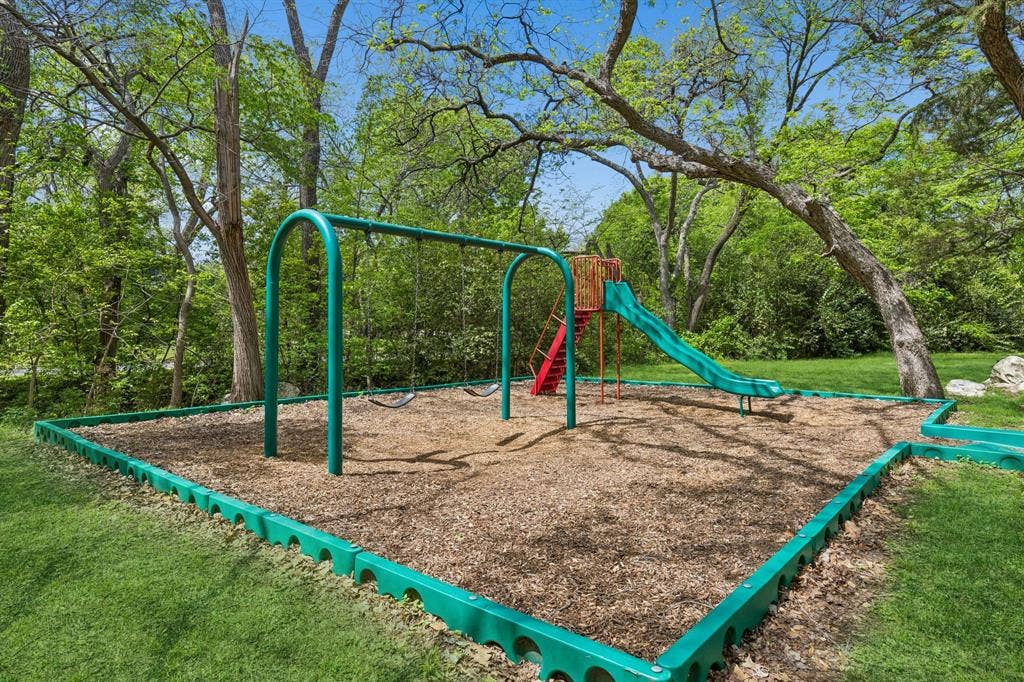 12124 Dixfield Drive, Dallas, TX 75218 Outdoor play area featuring a swing set, slide, and wood chip ground cover, bordered by green edging