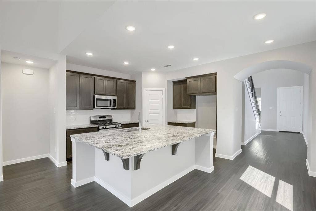 3925 Chesapeake Lane, Heartland, TX 75126 Kitchen featuring a large island with a stone countertop, dark wood-finish cabinetry, stainless steel appliances, and wood-finish flooring