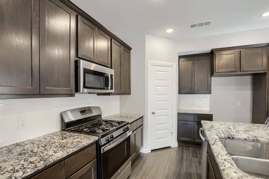 3925 Chesapeake Lane, Heartland, TX 75126 Modern kitchen featuring dark wood cabinetry, granite countertops, stainless steel gas range with overhead microwave, and dual undermount sinks