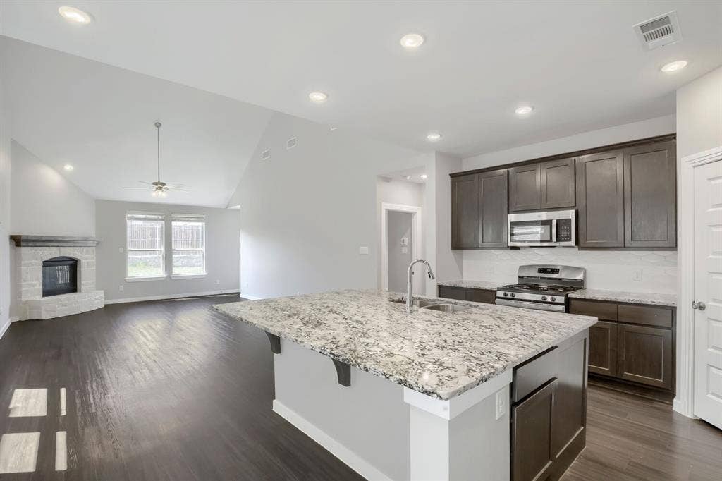3925 Chesapeake Lane, Heartland, TX 75126 Open-concept kitchen with a large granite island, stainless steel appliances, and dark wood-finish cabinetry