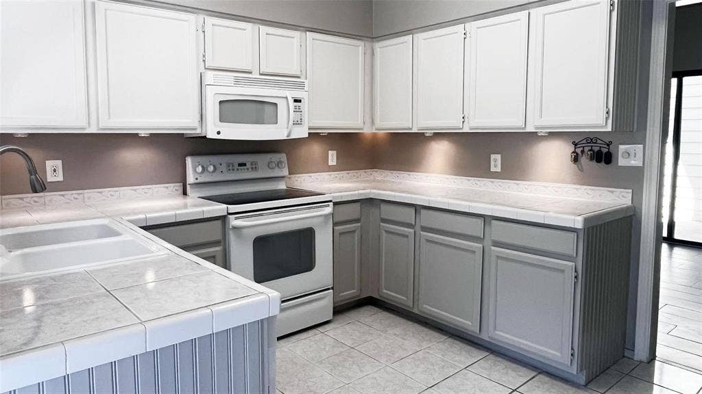 Kitchen featuring white upper cabinetry, gray lower cabinetry, tile countertops, a double basin sink, and tile flooring