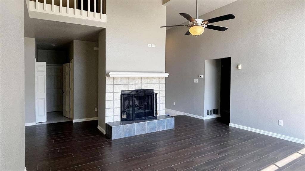 Vaulted ceilings, wood-finish flooring, a ceiling fan with integrated lighting, and a fireplace with a tile surround and hearth