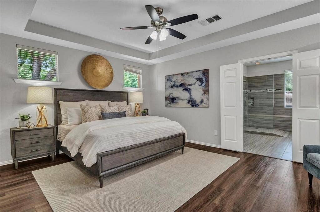 1601 Long Prairie Court, Allen, TX 75002 Tray ceiling with a ceiling fan, dark wood-finish flooring, two windows with blinds, and white double doors opening to a shower with glass enclosure