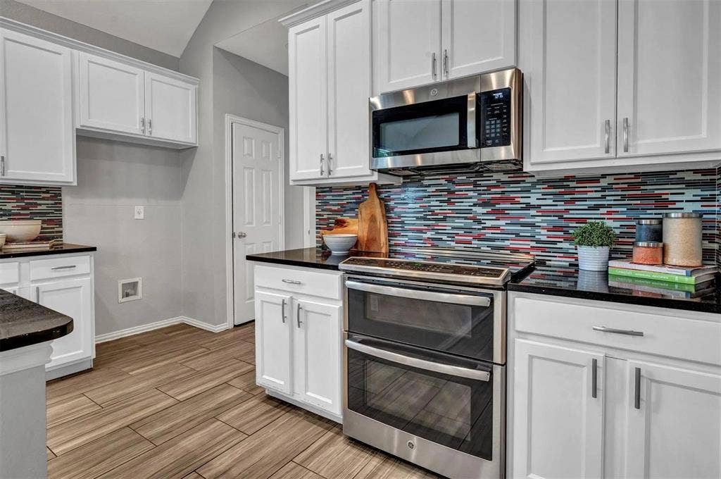 1601 Long Prairie Court, Allen, TX 75002 White shaker-style cabinetry, black countertops, stainless steel appliances, mosaic tile backsplash, and wood-finish flooring