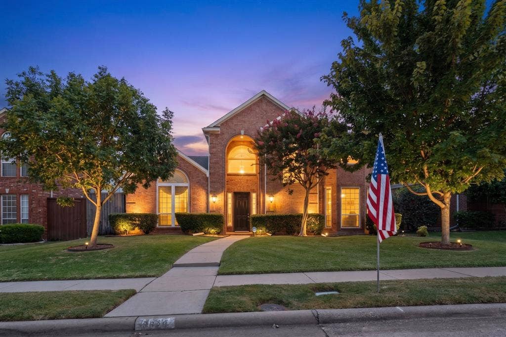 3820 Nash Lane, Plano, TX 75025 Brick exterior with arched entryway, mature trees, manicured lawn, and exterior uplighting