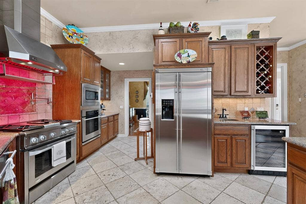 3820 Nash Lane, Plano, TX 75025 Gourmet kitchen featuring stainless steel appliances, a built-in wine rack, a beverage cooler, and extensive wood cabinetry