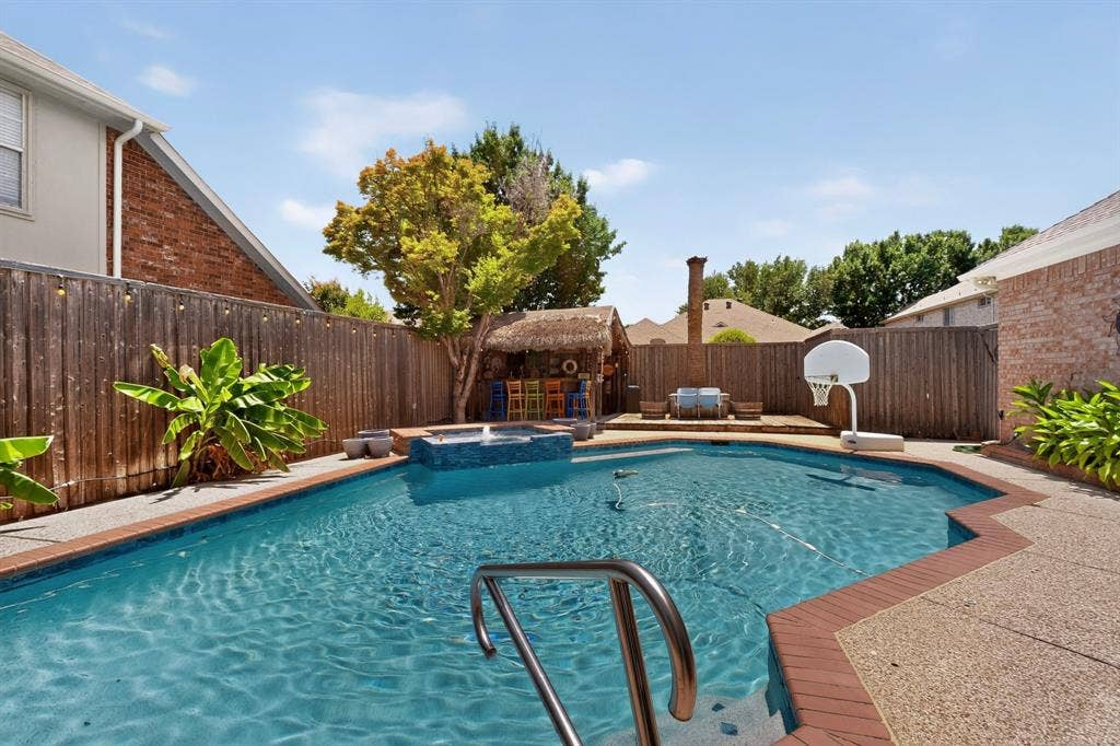 3820 Nash Lane, Plano, TX 75025 Resort-style backyard oasis featuring a sparkling in-ground swimming pool with integrated spa, brick decking, mature landscaping with tropical plantings, wooden privacy fencing, and a basketball hoop for recreational enjoyment