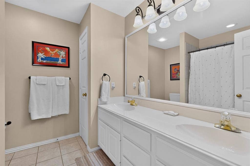 3820 Nash Lane, Plano, TX 75025 Double vanity with integrated sinks, large mirrored wall, multi-bulb vanity lighting, and tiled flooring