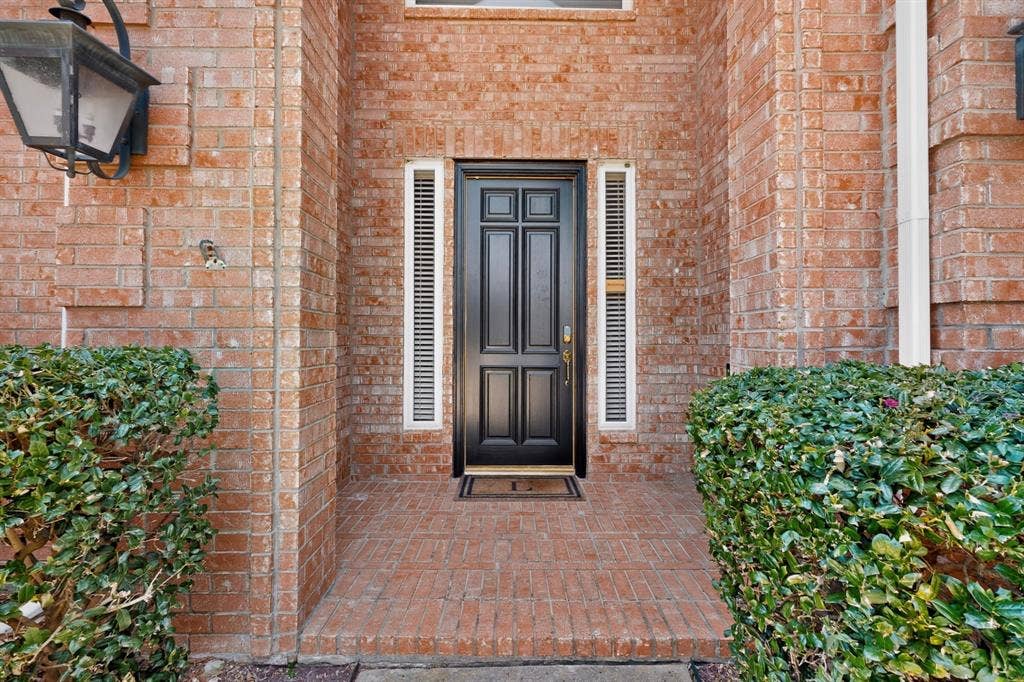 3820 Nash Lane, Plano, TX 75025 Elegant brick courtyard entry featuring a six-panel black lacquered door with sidelights, complemented by manicured hedge landscaping and traditional lantern sconce lighting