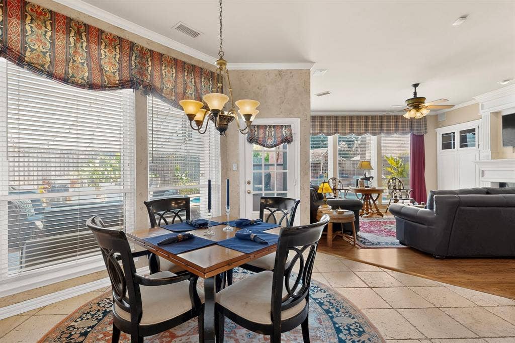 3820 Nash Lane, Plano, TX 75025 Tile flooring in the dining area with a brass chandelier, large windows with white blinds, and a built-in white media cabinet in the background