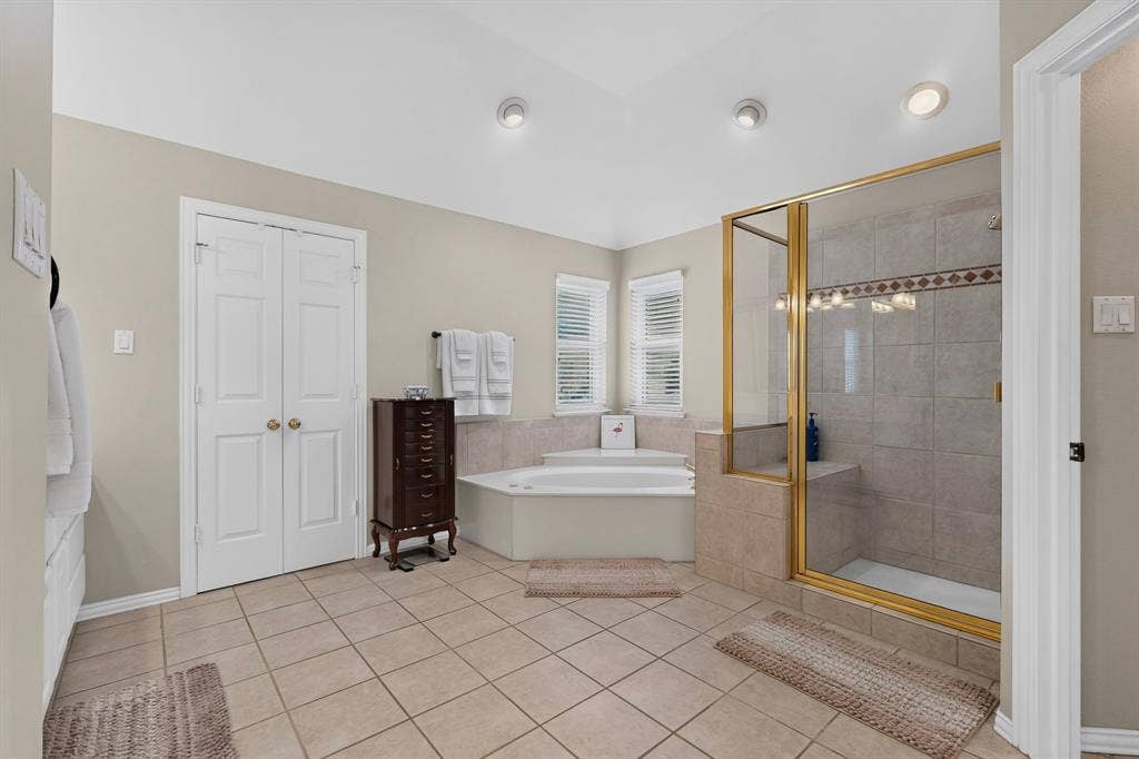 3820 Nash Lane, Plano, TX 75025 Corner soaking tub, separate tiled shower with glass enclosure, tiled flooring, recessed lighting, and white plantation shutters