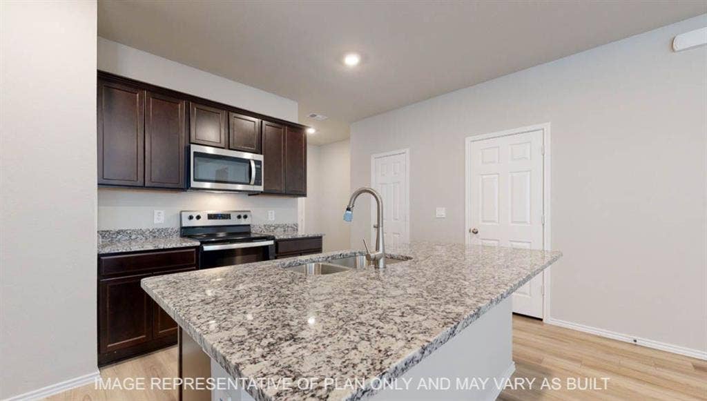 3016 Cyprian Road, Lorena, TX 76655 Kitchen island with integrated sink, dark wood-finish cabinetry, stainless steel microwave, and wood-finish flooring