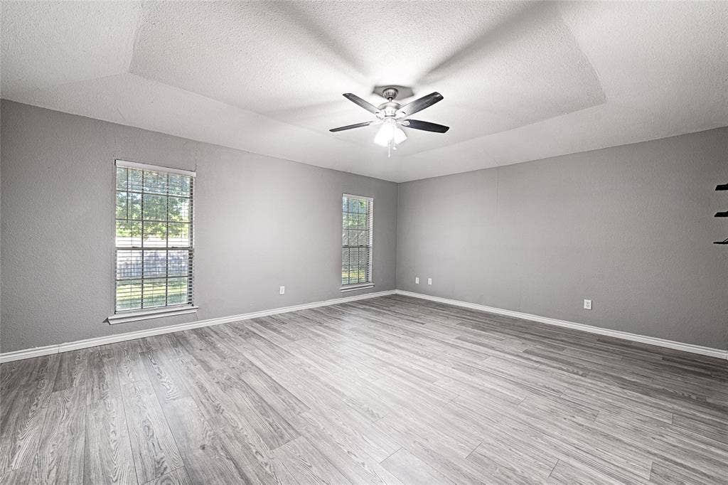 1223 Sequoia Drive, DeSoto, TX 75115 Expansive room featuring wood-finish flooring, two windows with blinds, a tray ceiling, and a ceiling fan with light fixture