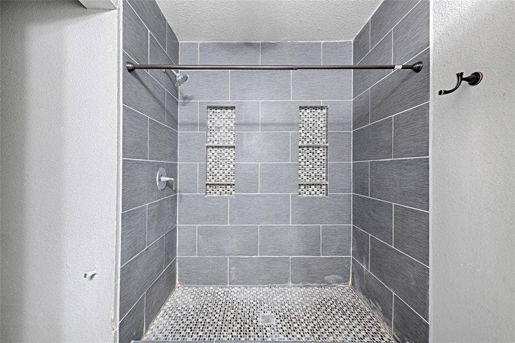 1223 Sequoia Drive, DeSoto, TX 75115 Tiled shower enclosure featuring rectangular gray wall tiles, mosaic tile shower floor, and two recessed mosaic tile niches