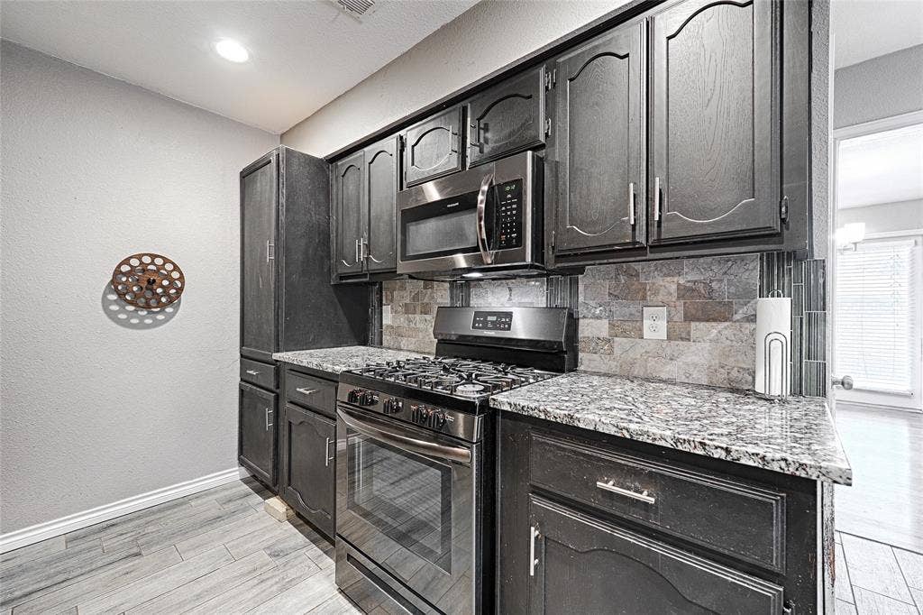 1223 Sequoia Drive, DeSoto, TX 75115 Kitchen featuring dark wood cabinetry, stainless steel appliances, speckled countertops, and a mosaic tile backsplash