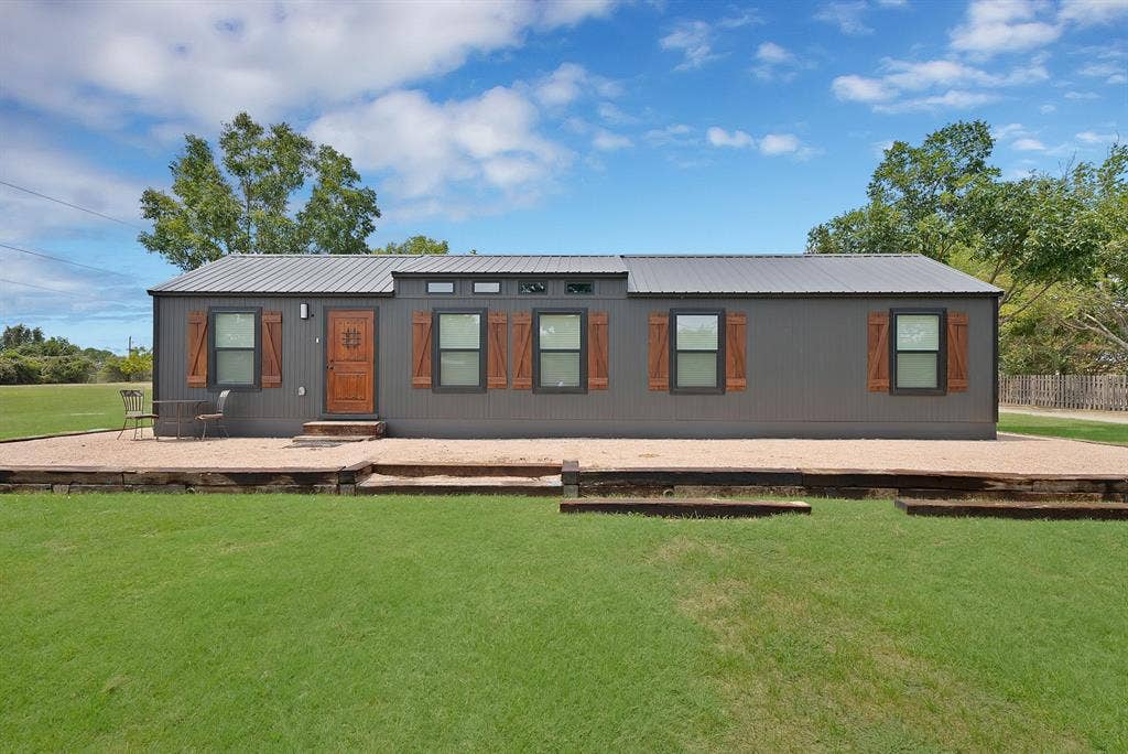 Gray exterior with a metal roof, wood-finish shutters, and a wood-panel entry door