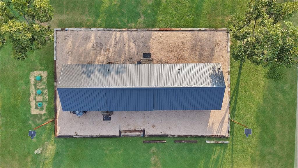 Corrugated metal roof, rectangular building, gravel lot, solar-powered lighting fixtures, surrounding green space