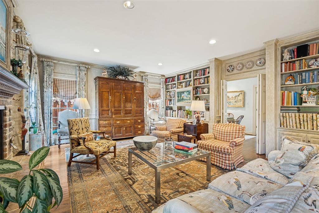 3418 Dartmouth Avenue, Highland Park, TX 75205 Sophisticated library and sitting room featuring extensive built-in bookshelves with decorative plate display, wood-paneled cabinetry, recessed ceiling lighting, patterned area rug, and multiple seating arrangements anchored by a glass-top coffee table