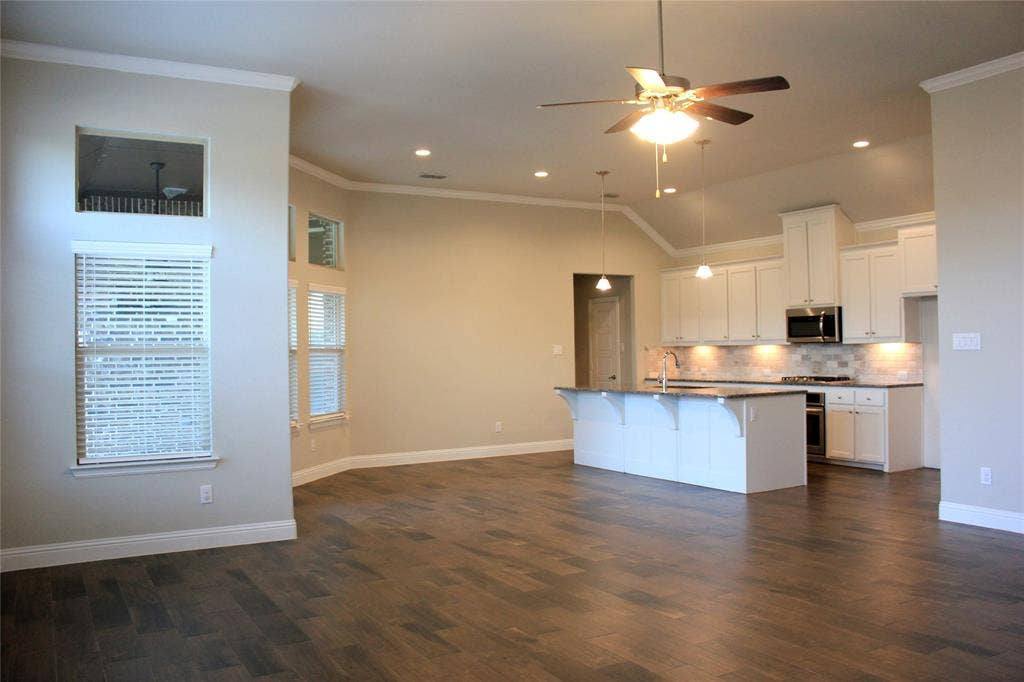 940 Parkside Drive, Argyle, TX 76226 Open-concept living area featuring wood-look flooring, vaulted ceilings, recessed lighting, and a kitchen with an island and white cabinetry
