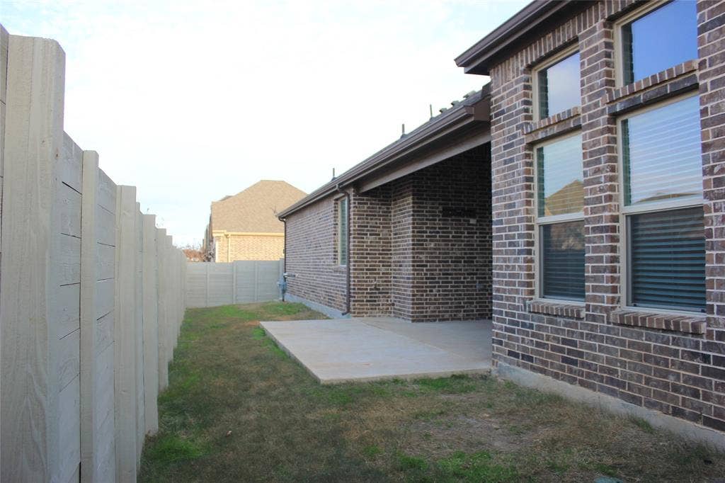 940 Parkside Drive, Argyle, TX 76226 Brick exterior with multiple windows, covered patio, concrete patio pad, and a privacy fence