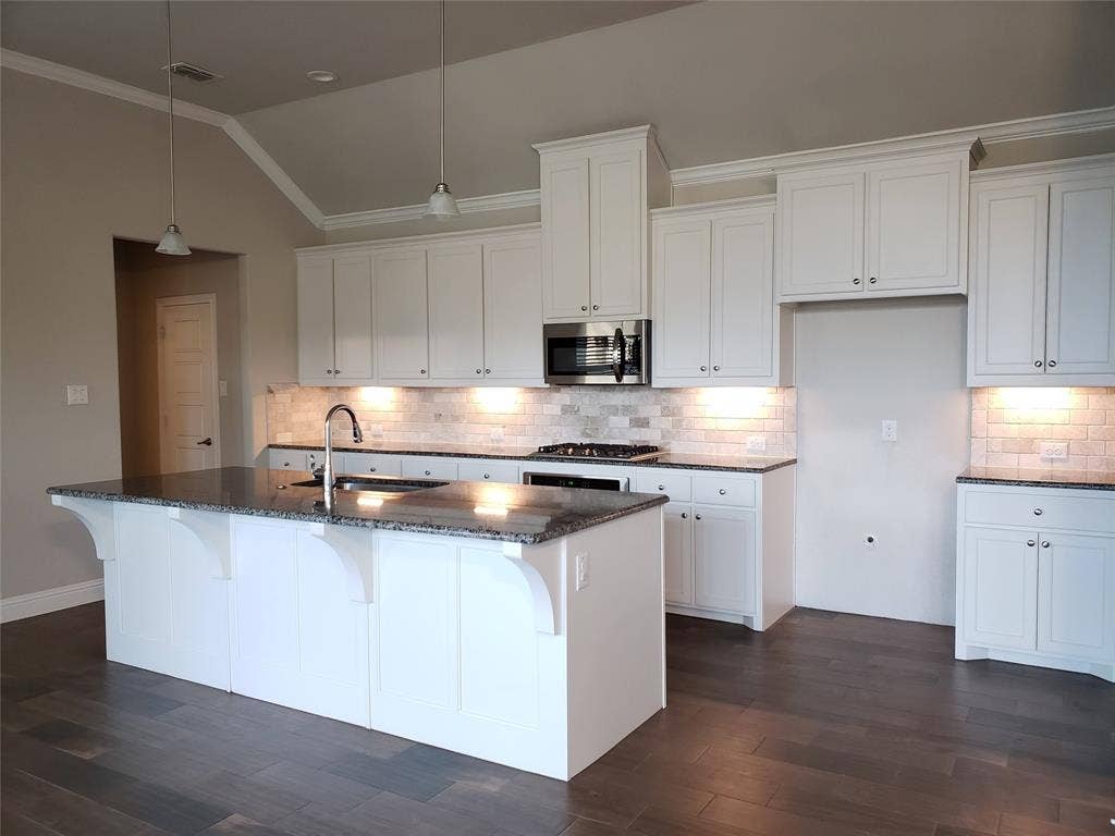 940 Parkside Drive, Argyle, TX 76226 Open-concept kitchen with a vaulted ceiling, wood-finish flooring, white cabinetry, granite countertops, and a subway tile backsplash