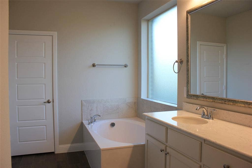 940 Parkside Drive, Argyle, TX 76226 Primary Bath Built-in soaking tub with tile surround, frosted privacy window, vanity with integrated sink, and framed mirror