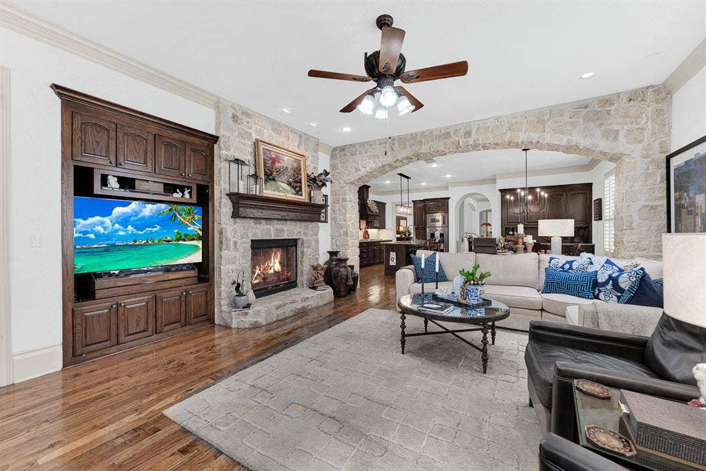 7032 PORTOBELLO Drive, Plano, TX 75024 A rustic stone fireplace with a raised hearth stands beside detailed custom cabinetry. Curl up by the flickering fire for a cozy movie night after a long day